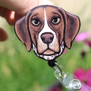 May include: A brown and white dog with brown eyes and a black nose. The dog is wearing a black and white patterned collar. The dog is a badge reel.
