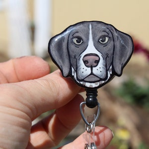May include: A black and white cartoon dog head on a retractable badge holder. The dog has brown eyes and a white nose.