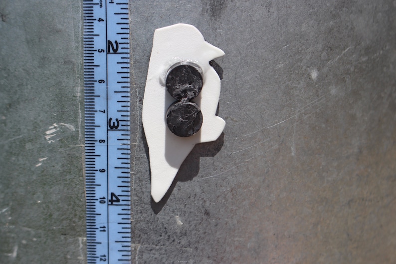 Op de afbeelding: Witte pingu&iuml;n-vormige magneet met twee ronde zwarte magneten aan de achterkant.
