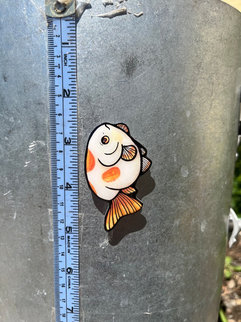 May include: A sticker of a cartoon fish with orange and white scales. The fish is about 2 inches long and has a smiling face.