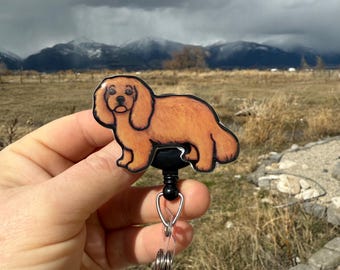 May include: A brown and black retractable badge holder with a cartoon illustration of a Cavalier King Charles Spaniel.