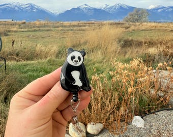May include: A black and white panda bear retractable badge reel. The badge reel has a black cord and a clear plastic clip. The text "No AI used in my Art" is visible in the background.