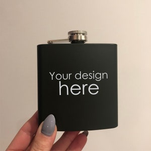 May include: A black metal flask with a silver lid and the text "Your design here" printed in white.