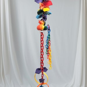 May include: A colorful hanging toy for sugar gliders, featuring a rainbow duck, multiple fabric loops, a chain with star-shaped beads, and two plastic rings with a blue and green ball.
