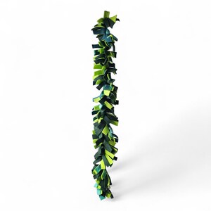 May include: A vertical garland composed of layered fabric strips in shades of green and blue. The strips are arranged in a staggered pattern, creating a textured, leafy appearance. The garland is likely for decorative purposes.