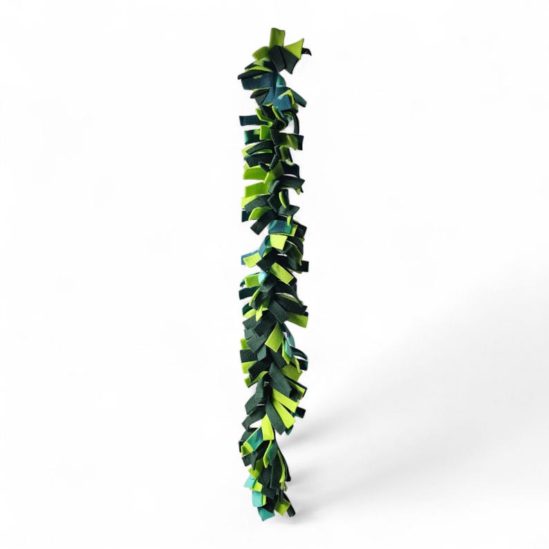 May include: A vertical garland composed of layered fabric strips in shades of green and blue. The strips are arranged in a staggered pattern, creating a textured, leafy appearance. The garland is likely for decorative purposes.