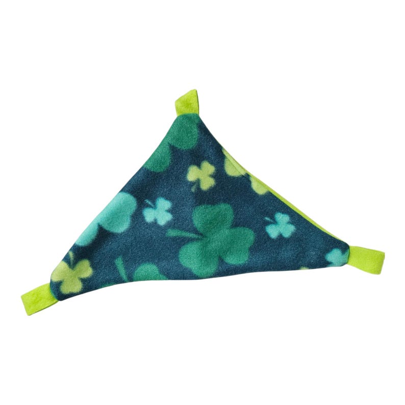 May include: A triangular pet accessory with a St. Patrick's Day theme. The dark teal fabric is patterned with various shades of green shamrocks. The edges are trimmed with a bright green fabric. This item is designed for small pets.