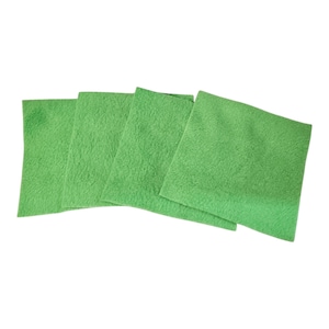 May include: Four square, bright green cloths are arranged diagonally across the frame. The cloths have a soft, textured appearance. The background is plain white.