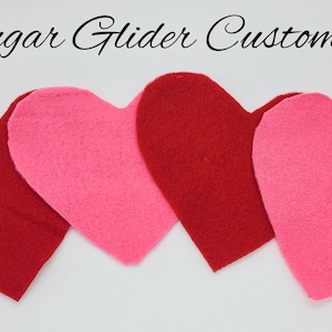 May include: Four felt hearts, two red and two pink, arranged in a row. The hearts are all the same size and shape. The text "Sugar Glider Customs" is written above the hearts.