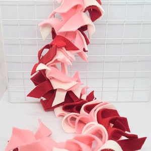 May include: A long, colorful, handmade toy made of red, pink, and white fleece fabric. The toy is designed for small animals like sugar gliders.