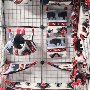 May include: A set of 10 fleece pet cage accessories in a red, white and blue buffalo plaid pattern. The accessories include hammocks, hideaways, and a hanging toy. The set also includes red and black fleece squares and a bag of colourful clips.