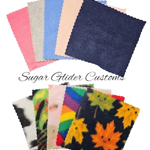 May include: Assortment of 10 different fleece fabric squares in various colours and patterns, including pink, blue, grey, black, rainbow, and a black fabric with orange maple leaves. The fabric squares are arranged in a semi-circle with the text "Sugar Glider Customs" in the center.