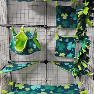 May include: A collection of pet accessories, including hammocks, tunnels, and hanging beds, in a teal and green clover pattern. The items are designed to fit inside a wire cage. The text "Sugar Glider Customs" is visible.