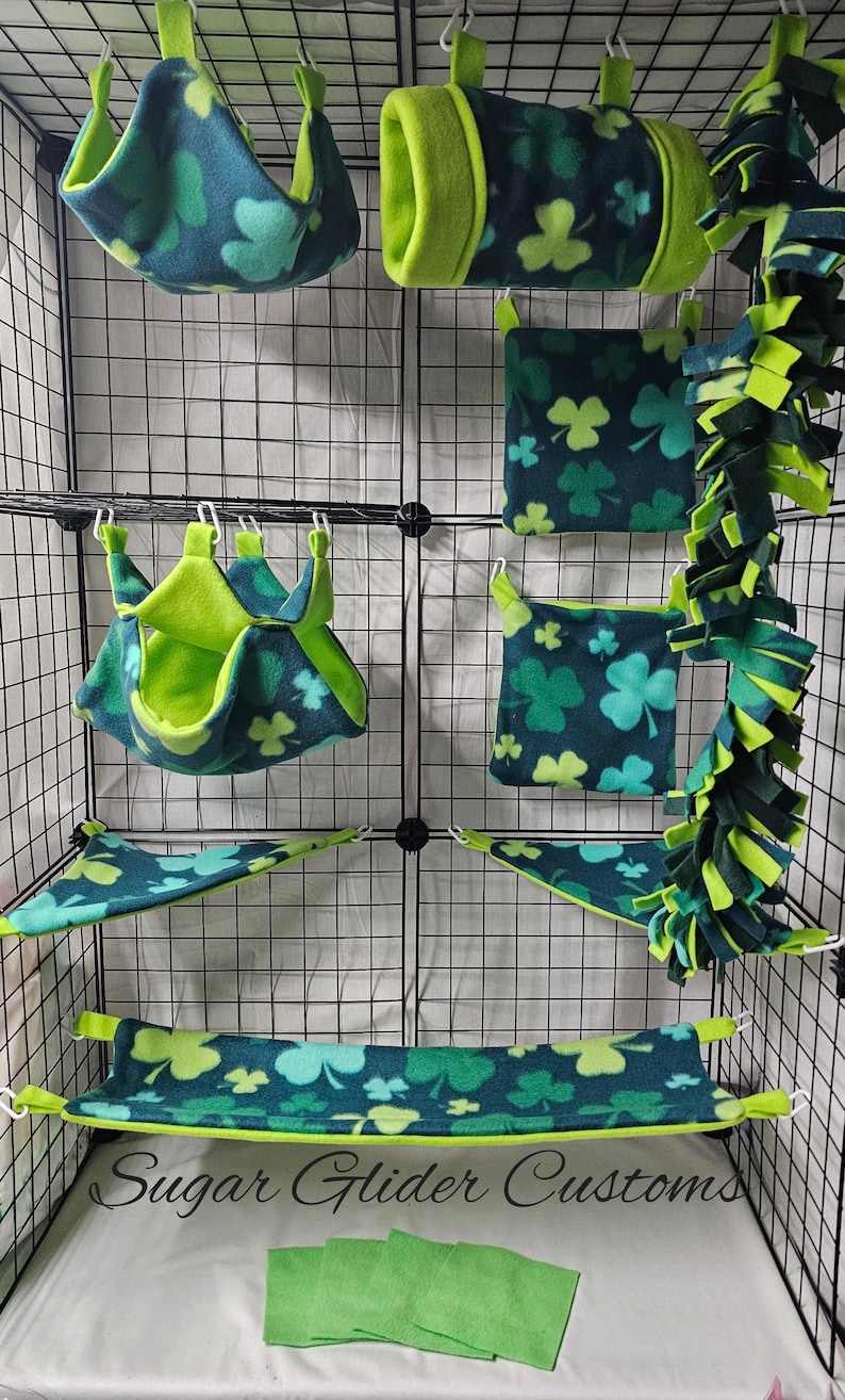 May include: A collection of pet accessories, including hammocks, tunnels, and hanging beds, in a teal and green clover pattern. The items are designed to fit inside a wire cage. The text "Sugar Glider Customs" is visible.