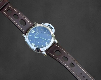 Könnte beinhalten: Eine luxuriöse Armbanduhr mit dunkelblauem Zifferblatt und silbernem Gehäuse. Die Uhr hat ein braunes Lederarmband mit weißen Nähten und ovalen Aussparungen. Das Zifferblatt zeigt die Zahl 12 und das Wort "PANERAI".