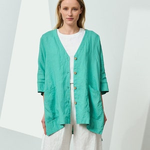 Op de afbeelding: Een turquoise linnen overhemd met knopen, lange mouwen en twee zakken. Het overhemd wordt gedragen over een wit T-shirt en een witte linnen broek.