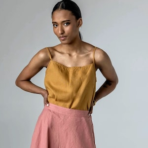 May include: A woman wearing a mustard yellow sleeveless top and a dusty rose linen skirt. She is wearing sandals and has her hair pulled back.