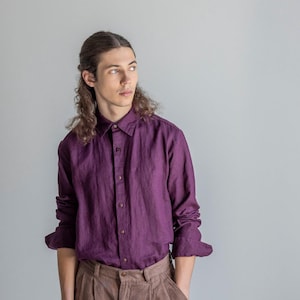 Op de afbeelding: Een pruimkleurig overhemd met knopen en een bruine plooibroek. Het overhemd met lange mouwen heeft een klassieke kraag en manchetten met knopen. De broek heeft wijde pijpen en wordt gecombineerd met donkerbruine instappers.