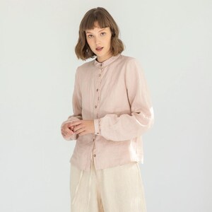 May include: A light pink linen shirt with a mandarin collar and button-down front is paired with cream-colored linen wide-leg pants. The outfit is completed with sandals. The clothing is made of a lightweight fabric.