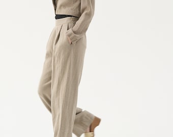 May include: A light tan linen suit, consisting of a cropped blazer and wide-leg pants. The blazer has a notched lapel and long sleeves. The pants have a high waist and pockets. The outfit is paired with wooden platform sandals. The model is wearing a black top.