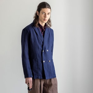 May include: A man wearing a dark blue linen blazer with a double breasted closure, brown linen pants, and brown leather shoes.