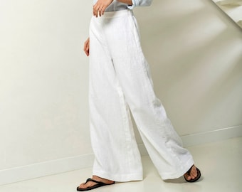 May include: A light blue long-sleeved linen top with a round neckline and rolled cuffs paired with high-waisted white wide-leg linen trousers. The outfit is completed with simple black thong sandals, creating a clean and coordinated look.