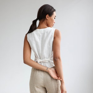 The back photo of linen buttoned vest with a v-neck. Back has an adjustable tie string. Here in white linen.
