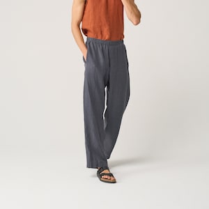 May include: A rust-coloured sleeveless tank top with a round neckline paired with loose-fitting charcoal grey trousers featuring an elastic waistband and side pockets, complemented by black open-toe sandals with two adjustable buckle straps.