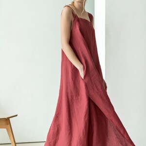 May include: A long, loose-fitting, sleeveless dress in a deep red color. The dress has a square neckline and a side slit. The dress is made of a soft, flowing fabric.