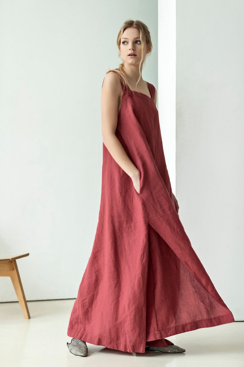 May include: A long, loose-fitting, sleeveless dress in a deep red color. The dress has a square neckline and a side slit. The dress is made of a soft, flowing fabric.