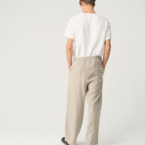 May include: A person wearing a white linen t-shirt and beige linen pants. The pants have a drawstring waist and a relaxed fit.