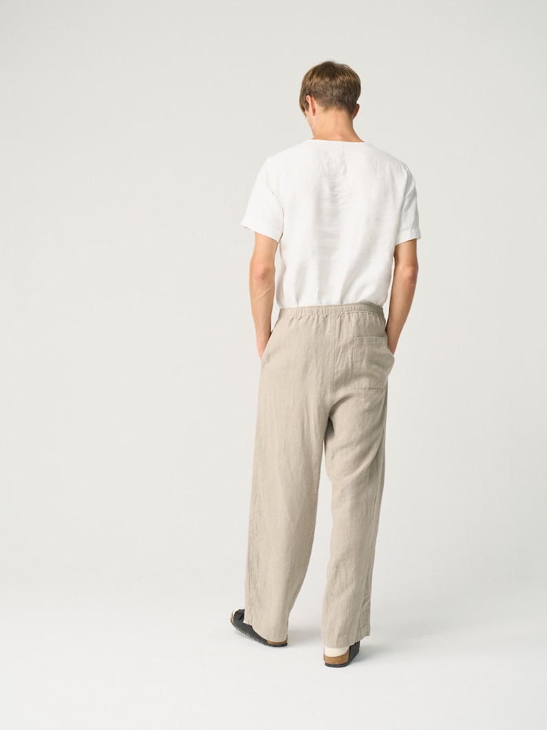 May include: A person wearing a white linen t-shirt and beige linen pants. The pants have a drawstring waist and a relaxed fit.