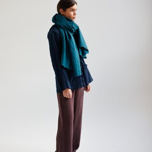 May include: A person wearing a teal scarf, navy blue shirt, and brown pants. The scarf is draped around the neck and shoulders. The pants are wide-legged. The outfit is simple and elegant.