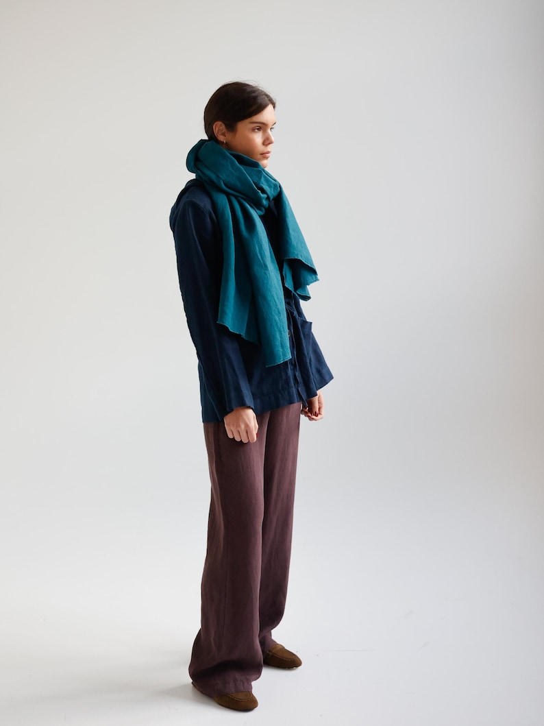 May include: A person wearing a teal scarf, navy blue shirt, and brown pants. The scarf is draped around the neck and shoulders. The pants are wide-legged. The outfit is simple and elegant.