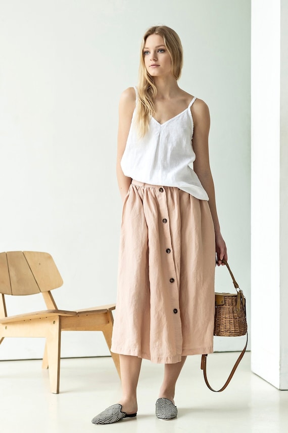 Stylish summer midi skirts: a model in a light top and blush midi skirt, accentuated by a woven bag and casual footwear.