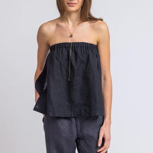 May include: A black strapless top with a gathered neckline and a gold necklace with a dark pendant. The top is paired with dark blue pinstripe pants. The outfit is simple and elegant.