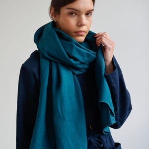 May include: A teal-colored linen scarf draped around the neck and shoulders. The scarf is a solid color and appears to be made of a soft, flowing fabric. The person in the image is wearing a dark blue outfit.