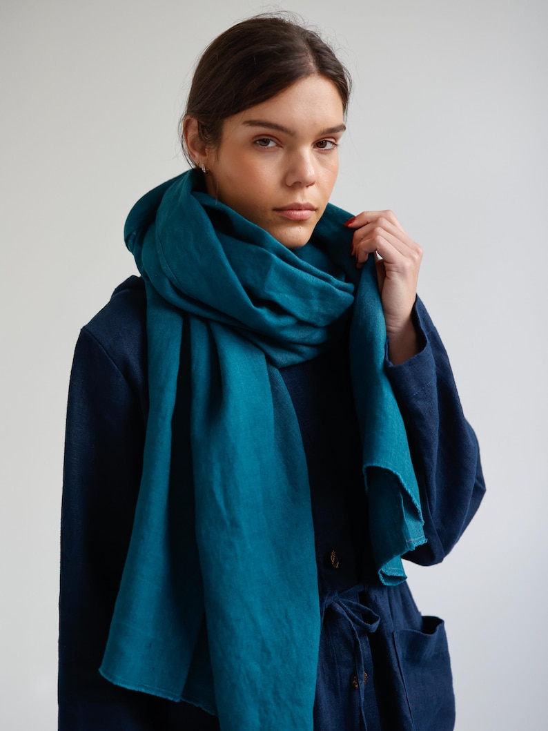 May include: A teal-colored linen scarf draped around the neck and shoulders. The scarf is a solid color and appears to be made of a soft, flowing fabric. The person in the image is wearing a dark blue outfit.