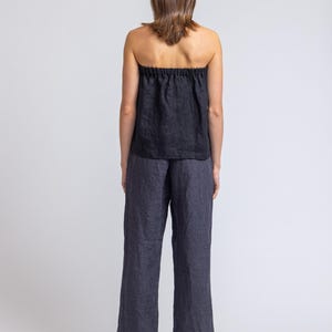 May include: Black strapless top and wide-leg pants. The top has a gathered neckline. The pants are a dark gray color. The outfit is made of a lightweight fabric, perfect for warm weather. The model is facing away from the camera.