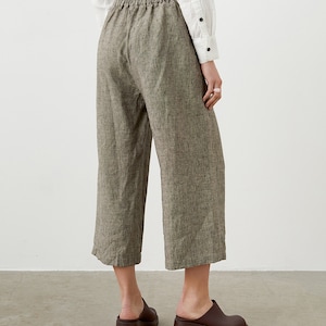 K&ouml;nnte beinhalten: Kurze Hose mit weitem Bein aus einem strukturierten, neutralfarbenen Stoff. Die Hose hat einen elastischen Bund und wird mit braunen Lederclogs kombiniert. Das Outfit wird durch ein wei&szlig;es Button-Down-Hemd erg&auml;nzt.