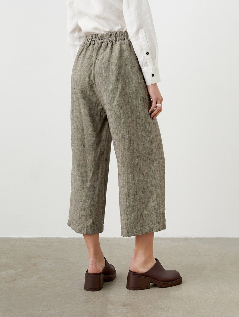 K&ouml;nnte beinhalten: Kurze Hose mit weitem Bein aus einem strukturierten, neutralfarbenen Stoff. Die Hose hat einen elastischen Bund und wird mit braunen Lederclogs kombiniert. Das Outfit wird durch ein wei&szlig;es Button-Down-Hemd erg&auml;nzt.