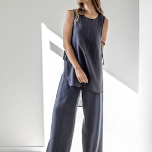 Puede incluir: Una mujer lleva una blusa sin mangas de lino azul oscuro y pantalones anchos a juego. La blusa tiene un dobladillo trasero ligeramente m&aacute;s largo y un detalle de corbata en el lateral.