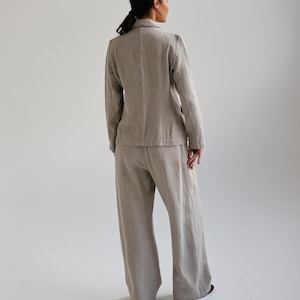 May include: A light beige linen blazer and wide-leg pants set. The blazer has a notched lapel and long sleeves. The pants are high-waisted and flowy. The outfit is made of a textured linen fabric.