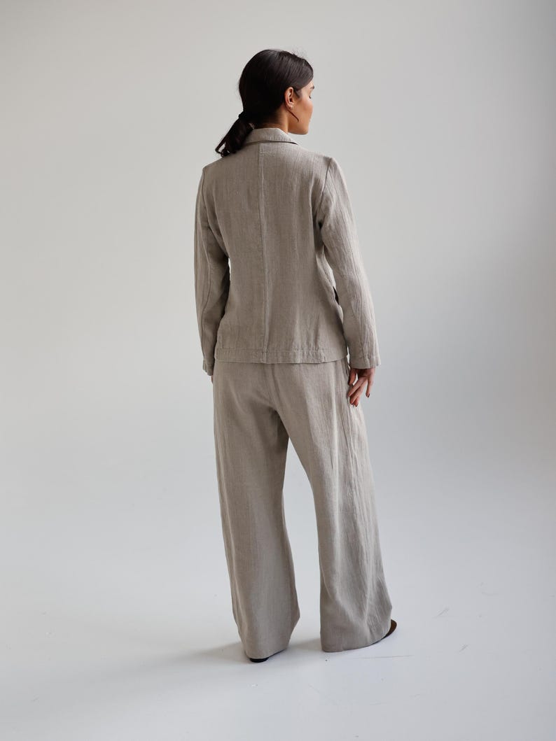 May include: A light beige linen blazer and wide-leg pants set. The blazer has a notched lapel and long sleeves. The pants are high-waisted and flowy. The outfit is made of a textured linen fabric.