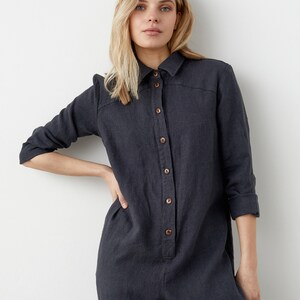 May include: A dark gray linen jumpsuit with a button-up front and long sleeves. The jumpsuit has a relaxed fit and a slightly cropped leg.