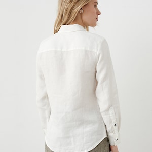 May include: A white linen shirt with long sleeves and a button-down front. The shirt has a classic collar and buttoned cuffs. The model is wearing the shirt with brown pants.