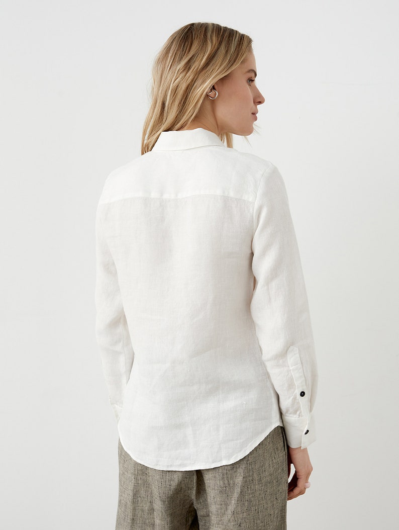May include: A white linen shirt with long sleeves and a button-down front. The shirt has a classic collar and buttoned cuffs. The model is wearing the shirt with brown pants.