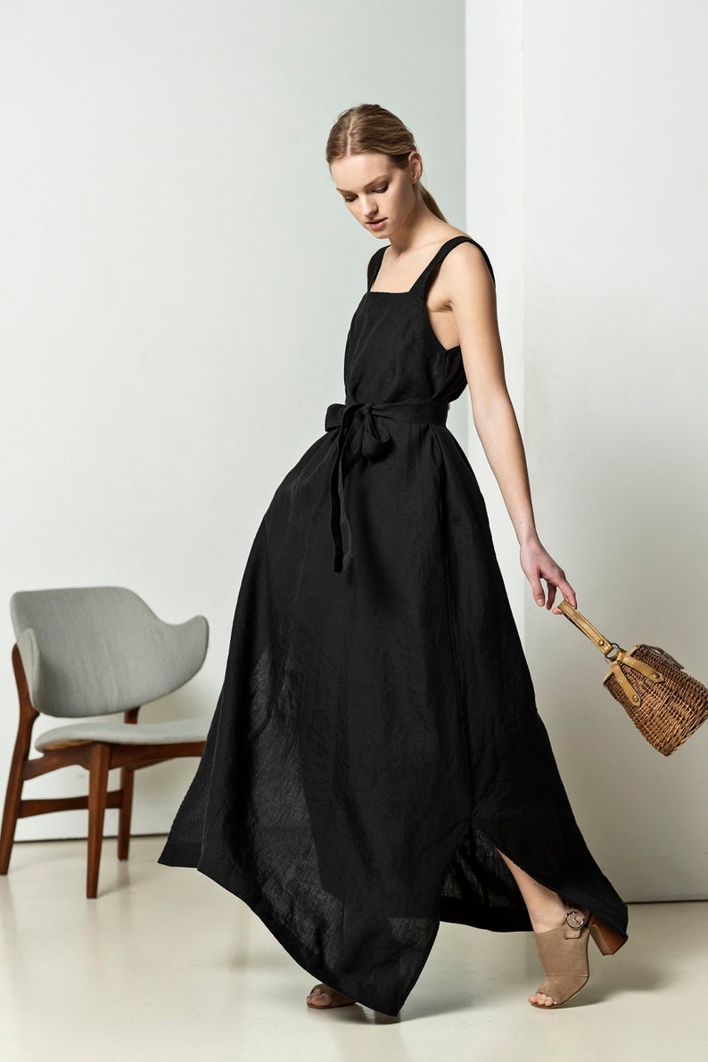 May include: A woman wearing a black linen maxi dress with a tie belt and a brown woven handbag.
