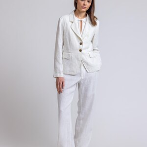 May include: A white linen blazer with a notched collar and two button fastening. The blazer has a relaxed fit and is paired with matching white linen trousers.