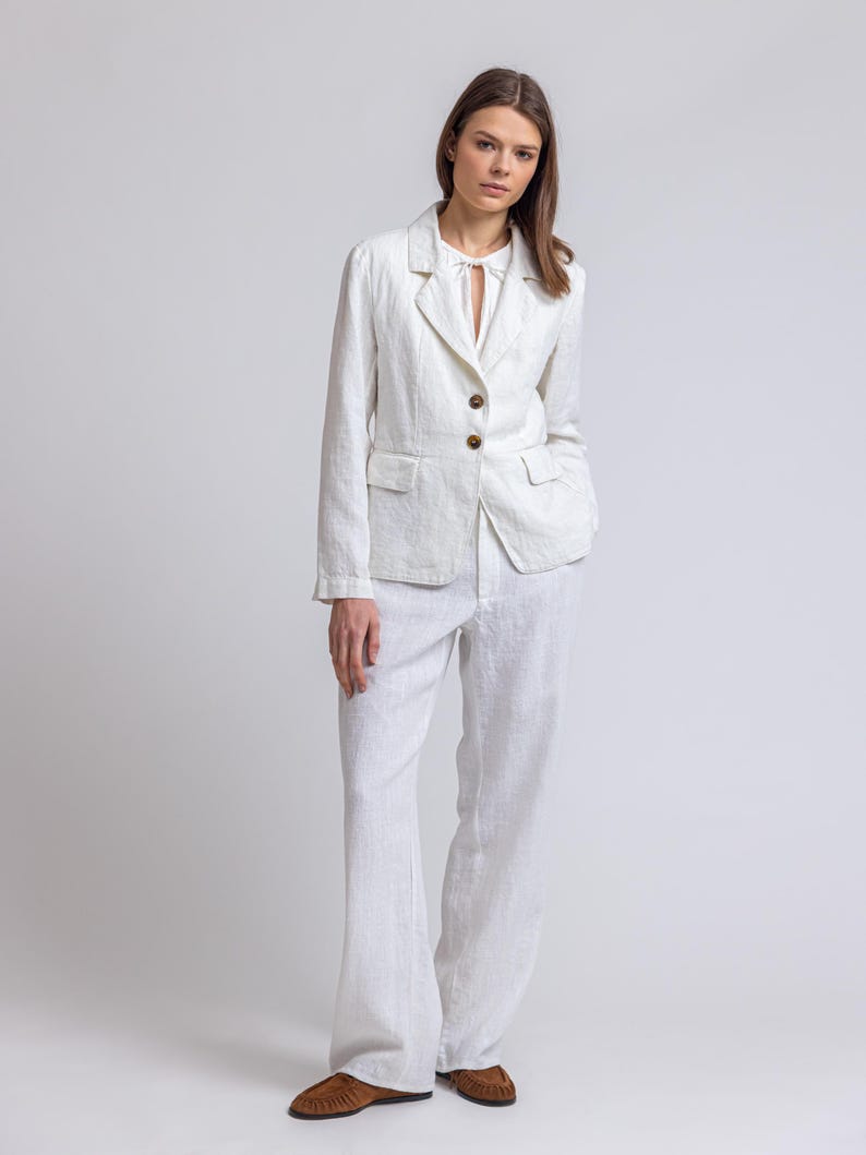 May include: A white linen blazer with a notched collar and two button fastening. The blazer has a relaxed fit and is paired with matching white linen trousers.